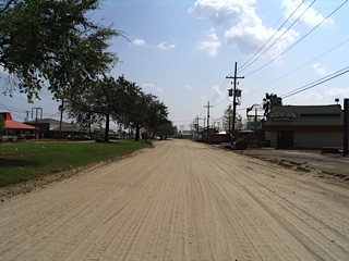 damaged and dirty road with homes to the sides